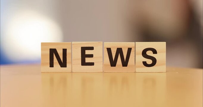 Wooden blocks spelling the word NEWS arranged in a row on a reflective surface.