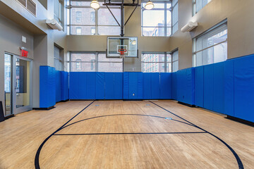 Empty indoor basketball court with hardwood floor and blue padded walls © nagelsphoto