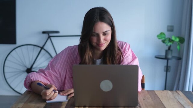Focused woman housewife seated at table writing down useful information, phone number or address of services founded in internet, groceries shopping list, do routine home work using personal organizer