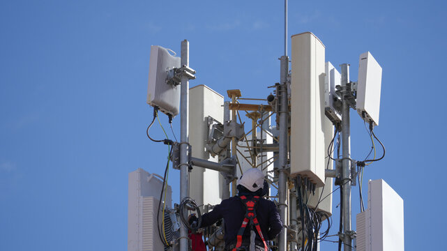 Worker wearing safety harness, helmet, maintaining cellular infrastructure, installing modern 5g antenna and connectivity equipment