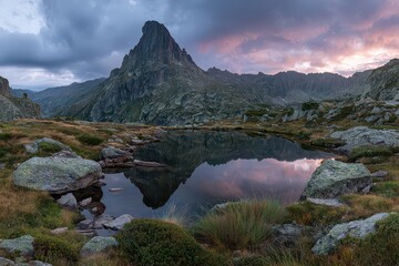 Naklejka premium Jagged Mountain Peak Reflecting in Calm Alpine Lake Under Cloudy Sky at Dusk