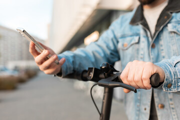 Close up of a man hand using a smartphone on the background of an electric scooter handle.