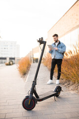 Young and handsome man using tablet device standing in the background of an electric scooter. Driving an ecological mode of transport.