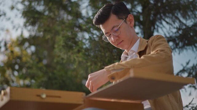 artist opening wooden paint box outdoors, unpacking supplies onto easel, checking brushes and palette, sunlight catching canvas edge, hands steady in preparatory moment, street art energy
