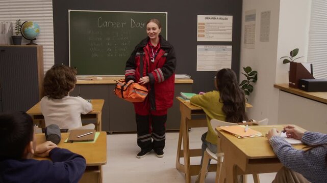 Zoom in shot of smiling young woman as female paramedic dressed in full uniform and gear speaking to group of children in class while giving presentation on career day in school, copy space