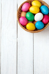 A basket of colorfull Eastereggs, on a white wooden background.
