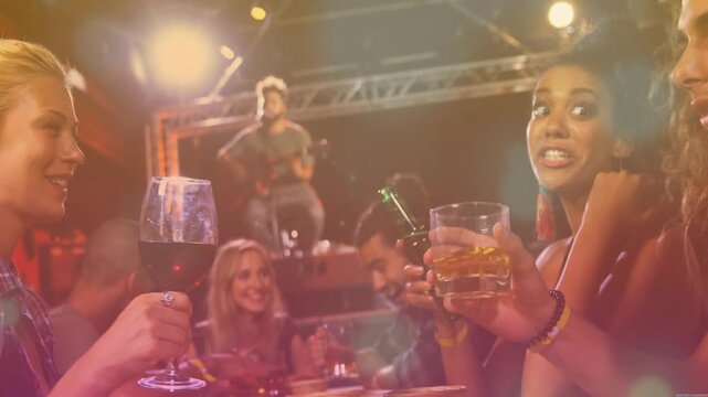 Musician playing guitar spurring friends raising wine glass and whiskey tumbler toasting live music