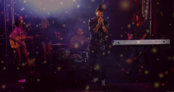 Lead vocalist stepping to center gripping mic, band performing music, sparkles floating over band