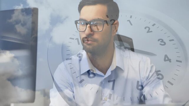 Male worker reaching keys and typing, glancing at screen, clock or clouds overlay marking office tim