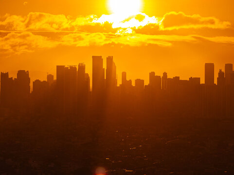 Manila city skyline glowing in warm golden hour sunlight, casting a captivating silhouette against a backdrop of vibrant orange clouds during sunset