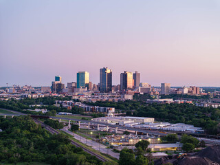 Fototapeta premium Aerial view of Fort Worth, Texas at dusk, vibrant cityscape, prominent skyscrapers, modern low residential buildings, active rail yard, and lush greenery