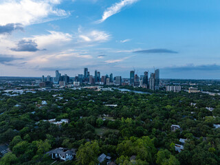 Obraz premium Austin, Texas skyline stands tall above lush greenery at dusk, showcasing coexistence of cityscape and nature under a partly cloudy sky