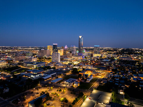 Oklahoma City's stunning skyline with Devon Energy Center emerges in the twilight, showcasing a lively urban scene with glowing buildings and busy streets