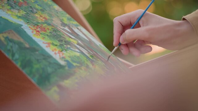 closeup hand adding fine highlights on canvas evening sunlight creates warm bokeh small sable brush refining tree branches and foliage vibrant pigment layers careful brushwork focused artist