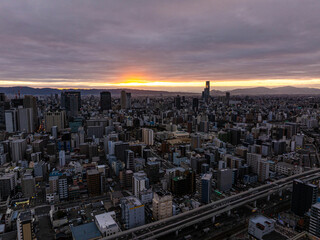 Fototapeta premium Beautiful golden hour sunrise over Osaka's urban skyline, with mountains in the distance and a highway running through the cityscape