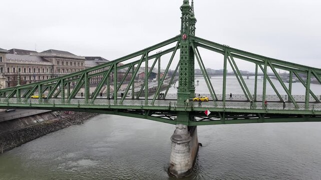 Slow camera pan moving rightwards along the iconic green steel structure of the Liberty Bridge in Budapest, featuring its Art Nouveau lattice and the Danube River