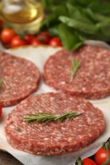 Uncooked meat patty with rosemary, tomatoes, lettuce and oil on table, closeup