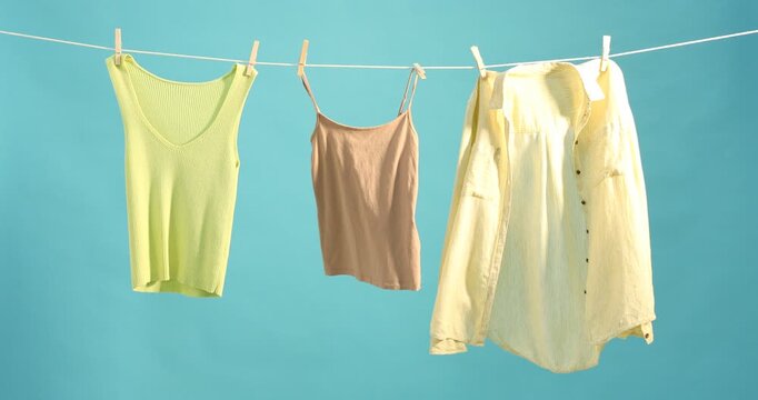 Different clothes drying while hanging on clothesline against light blue background