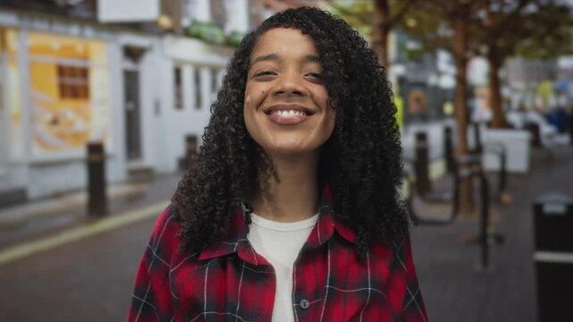 Woman with curly hair sticks out her tongue on a vibrant city street with blurred storefronts; cheeky mischief.
