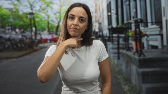 Woman pointing index finger to camera on street, white tshirt with visible hand and forearm gesture near face conveying emphasis; confidence.