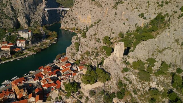 Epic aerial view of Mirabella Fortress tower on a steep cliff above Omis Old Town, Cetina river canyon and Adriatic sea, Croatia, 4K