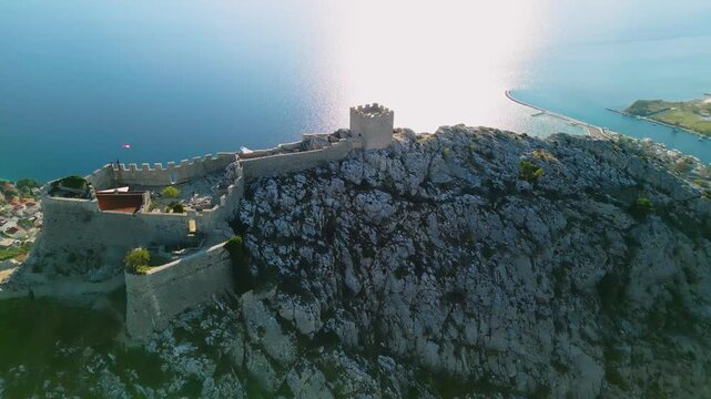 Epic aerial view of Mirabella Fortress tower on a steep cliff above Omis Old Town, Cetina river canyon and Adriatic sea, Croatia, 4K