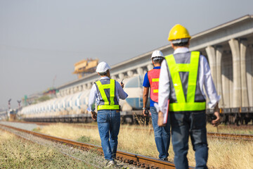 Railway engineers walking along track during infrastructure inspection, Transportation workers inspecting freight train and rail line, Rail maintenance team conducting safety check on railway tracks
