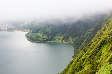 Obraz premium Lake surrounded by green hills and fog at Sete Cidades, San Miguel, Azores. Lush forested landscape in the background. A volcanic crater lake in Portugal.