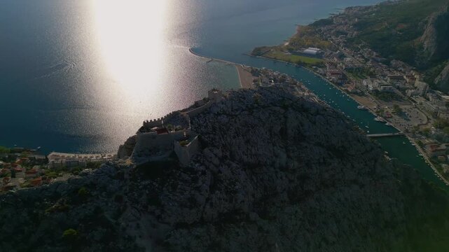 Epic aerial view of Mirabella Fortress tower on a steep cliff above Omis Old Town, Cetina river canyon and Adriatic sea, Croatia, 4K
