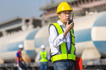 Railway supervisor using walkie talkie during train inspection at freight yard, Engineer coordinating rail logistics with radio communication, Industrial safety officer monitoring railway operations