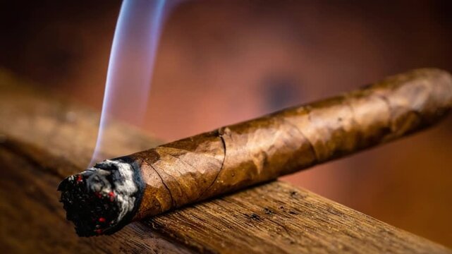 Close-up of a lit cigar with smoke rising on a wooden surface