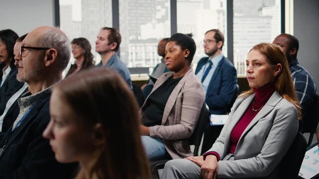 Businesswoman raising hand, asking questions and engaging in debate with microphone during presentation. Diverse group of professionals and executives attending corporate event. Camera A.