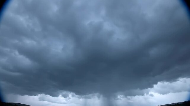 Dark, stormy clouds unleash heavy rain over a distant landscape, creating a dramatic and intense weather scene under an ominous sky.