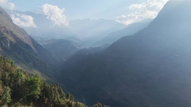 Horizontal aerial shot flying forward through a vast and deep mountain valley. Capturing the layered mountain ranges extending into the distance under a clear sky. Cinematic drone travel through a rug