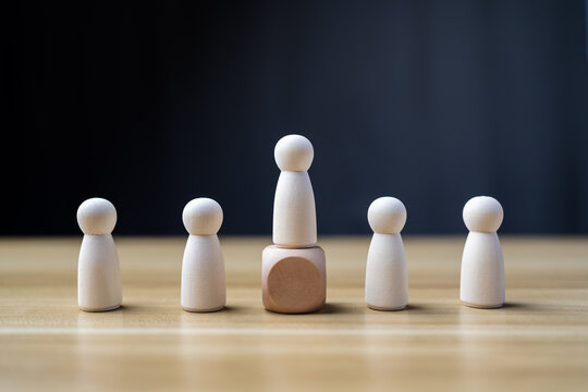 Leadership concept with one tall wooden peg doll standing on block above group. Success and promotion concept