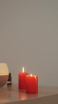 red candles on wooden table, lamp two lit red pillars beside ceramic diffuser bowl create warm glow on varnished surface minimalist spa setup evokes calm preparation for massage or microcurrent