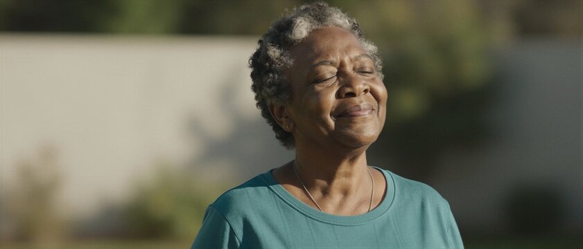 Senior Black woman practicing mindful deep breathing and basking in warm sunlight, focusing on holistic wellness and healthy aging for longevity.