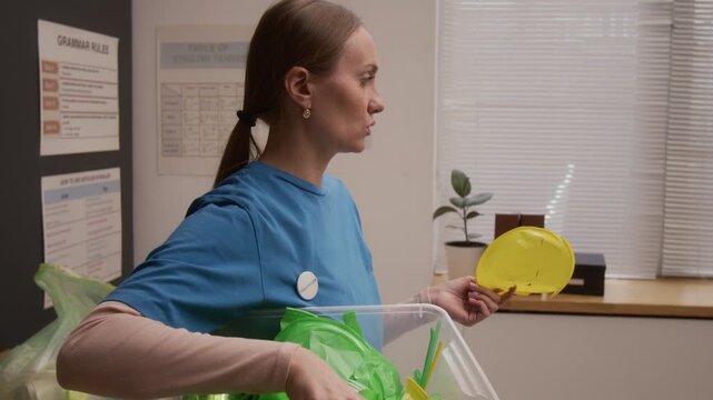 Close up shot of young woman as environmental educator holding bin with plastic waste while explaining sorting and recycling during presentation on career day in school classroom, copy space