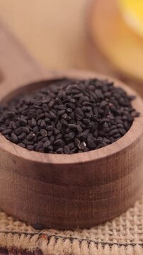 Black cumin seeds in a wooden bowl on a burlap surface