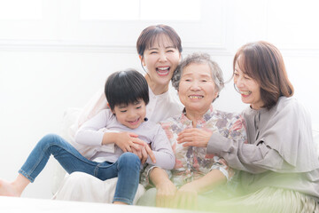 Obraz premium 逆光の綺麗な部屋で祖母と母と子ども(ひ孫）が笑顔で抱き合う四世代家族、親子の幸せな記念写真 カメラ目線 