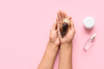 Female hands with snail and cosmetics on pink background © Pixel-Shot