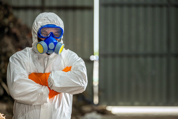 Portrait of confident scientist in hazmat suit for safety control standing with arms crossed pose at waste management plant. Hazardous trash inspector in PPE posing at toxic garbage pile site.