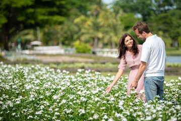 Fototapeta premium Romantic couple enjoying and looking white flower field together emotional bonding moment between couple outdoors. Happiness two people male smiling and female touching nature in garden