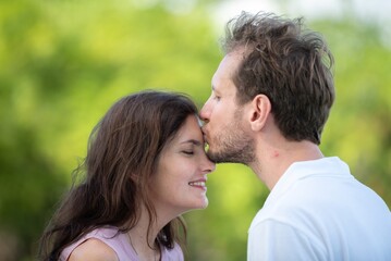 Obraz premium Affectionate man kissing woman forehead tender emotional love and trust between couple peaceful romantic gesture in outdoors. Happy couple sharing gentle intimate moment in garden.
