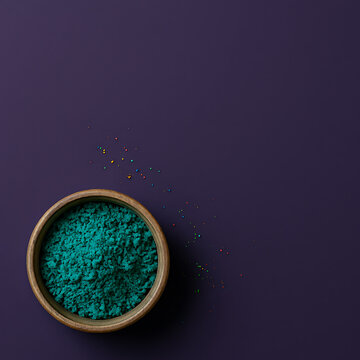 Minimalist Top View of Teal Holi Powder in a Bowl on Solid Deep Purple Background, Modern Artistic Flat Lay with Copy Space for Creative Design