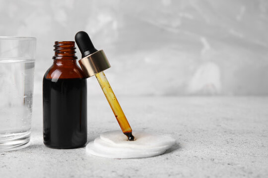 Bottle with iodine, pipette, cotton pads and glass of water on grey grunge background, closeup