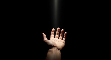 Human hand reaching up into a narrow beam of light against a dark, black background, symbolizing hope or divine intervention.