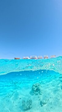 Vertical shot of half underwater view of tourist yachts anchored in turquoise lagoon during snorkeling excursion in Ras Mohammed National Park