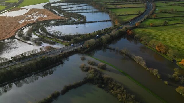 Drone view pullout of Malton bypass A64 dual carraigeway with cars driving runs over a flooded River Derwent and surrounding green fields on sunny winter day