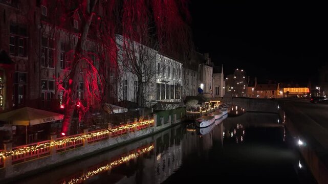 Night footage of the Christmas-decorated canal in Bruges at Nepomucenus Bridge, featuring festive lig